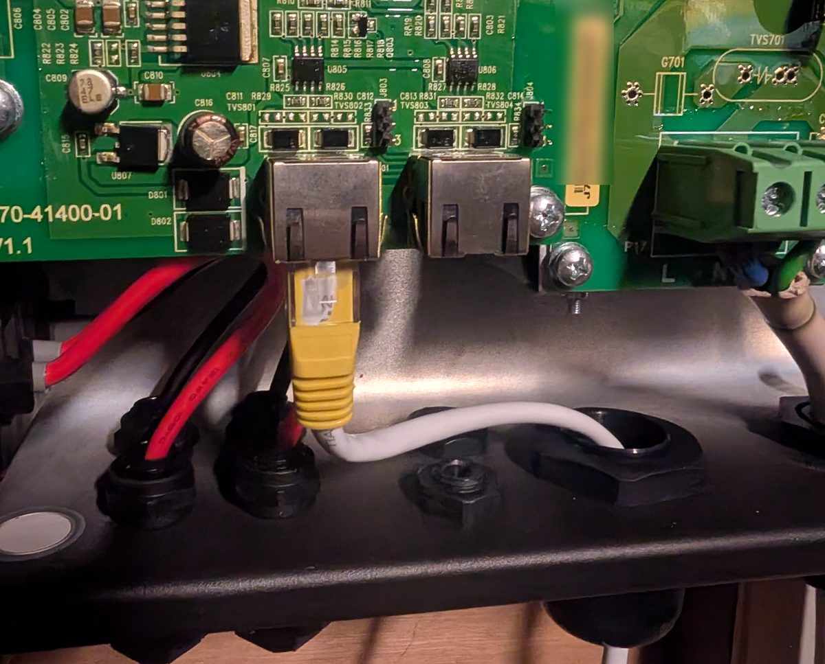 A yellow RJ45 plug in one of the two network sockets on the inverter's circuit board, with its white cable running out through a cable gland in the base.